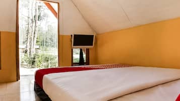 A room with a bed, a television mounted on the wall, and a view of trees and greenery outside.