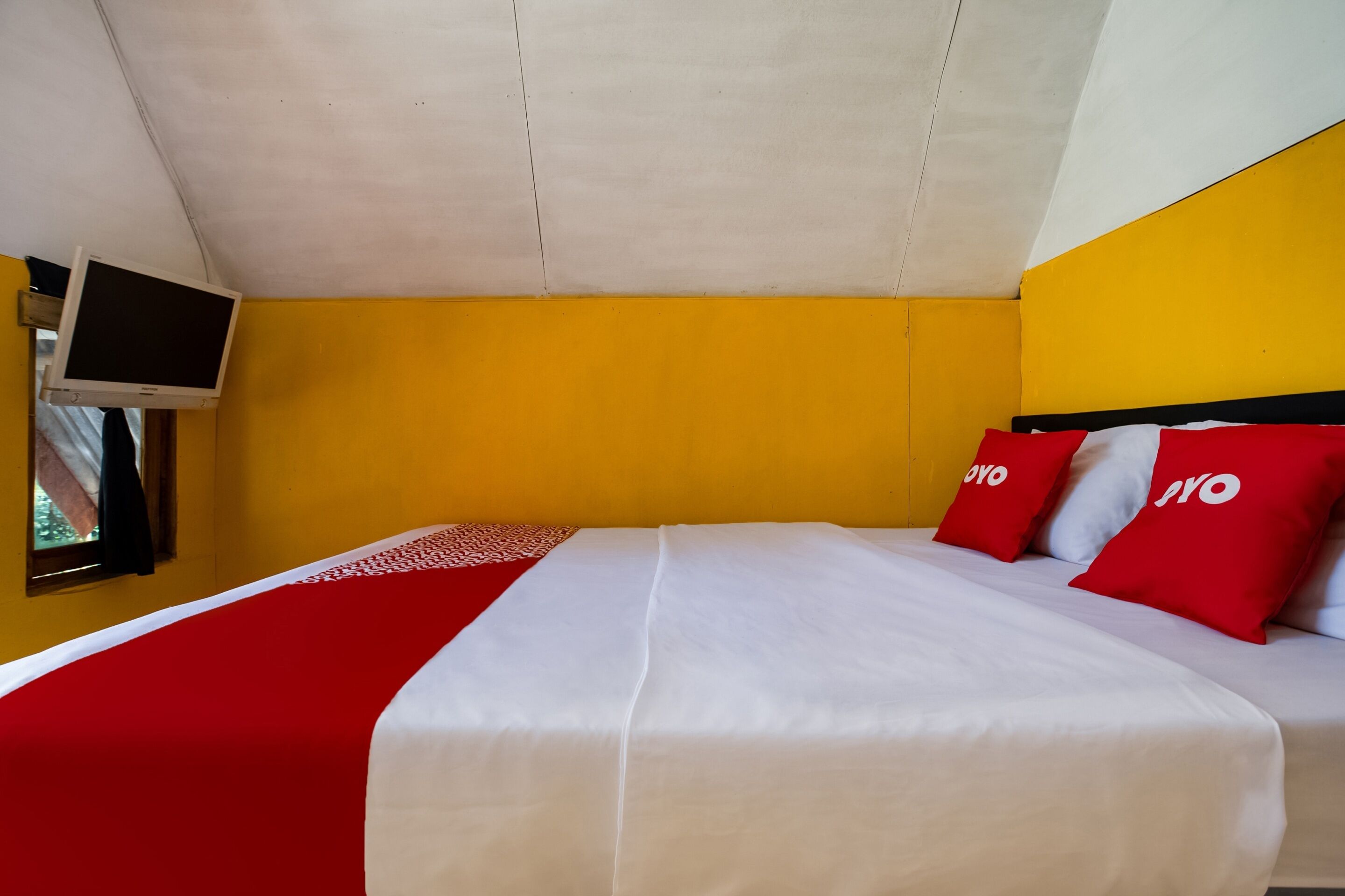 Habitación de hotel con cama, televisor montado en la pared y ventana con vistas.