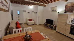 Una sala de estar con sofá, televisor, armarios de madera y una zona de comedor con mesa.