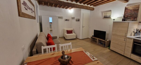Ein Wohnzimmer mit Sofa, Fernseher, Holzschränken und einem Essbereich mit Tisch.