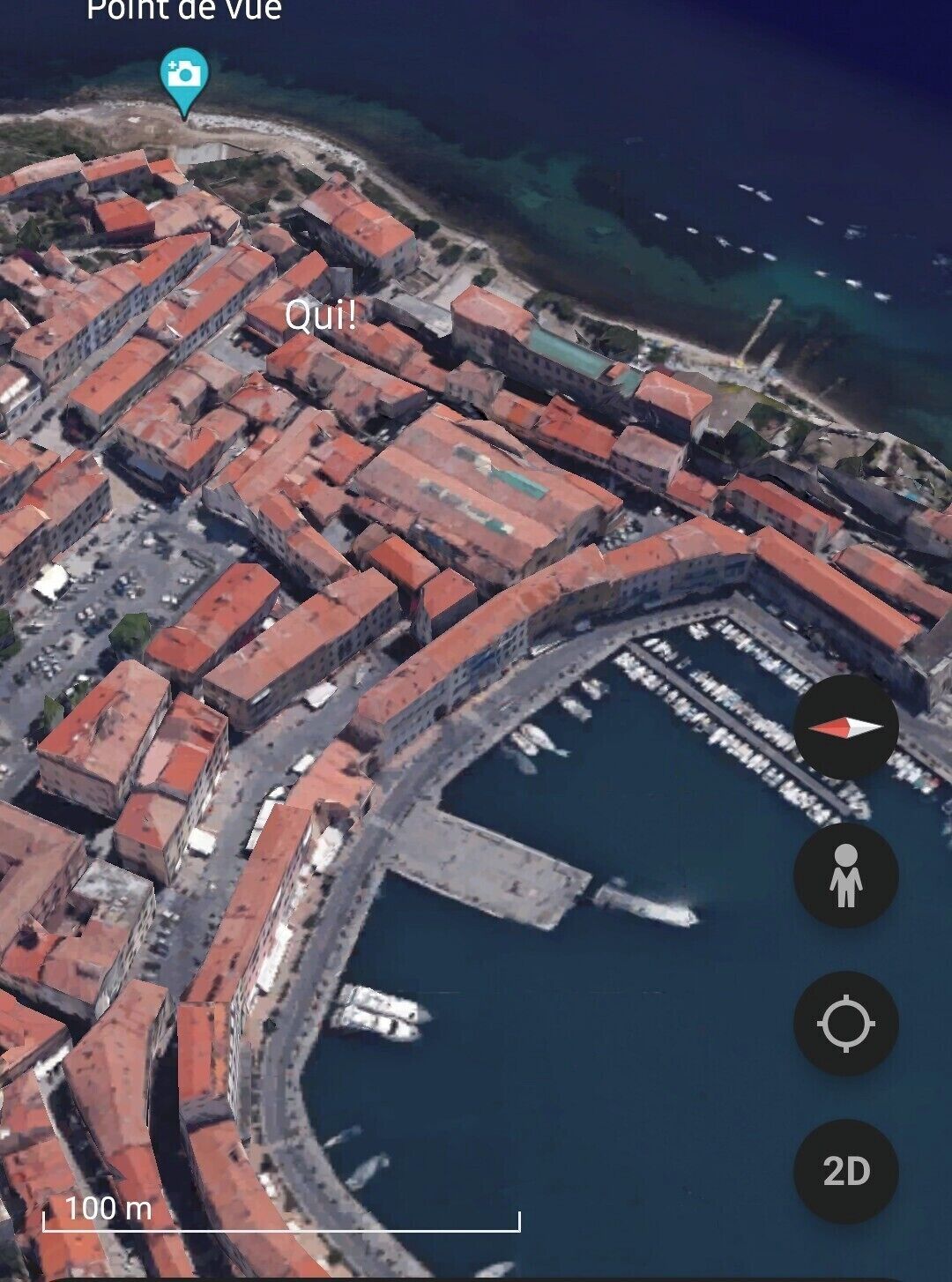 Luchtbeeld van een kustplaatsje met rode daken, een jachthaven en een helder uitzicht op zee.