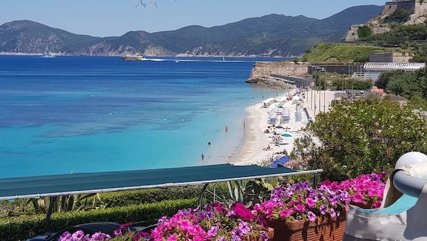Vista costera con playa, aguas azules cristalinas y montañas al fondo.