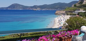 Blick auf die Küste mit Strand, klarem blauen Wasser und Bergen im Hintergrund.
