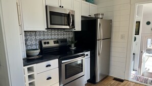A modern kitchen with white cabinets, stainless steel appliances, and a wooden floor.