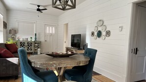 A dining area with a round wooden table, two blue upholstered chairs, and a white ottoman.