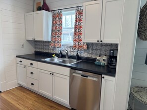 A kitchen with white cabinets, a stainless steel dishwasher, a double sink, and a coffee maker.