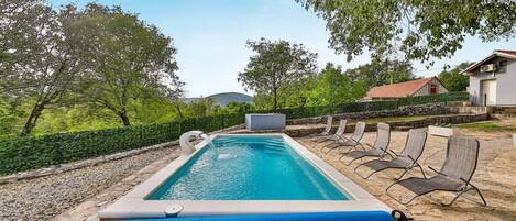 Una piscina rectangular con una cubierta azul, rodeada de sillas de descanso y un camino de piedra.