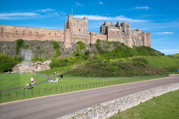 A historic castle on a hill with a paved road in the foreground. - Castle View - sleeps 16 guests in 8 bedrooms (Bamburgh)