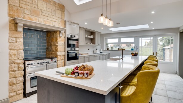 Een moderne keuken met een accentmuur van steen, ingebouwde apparatuur en een lang eiland met barstoelen.