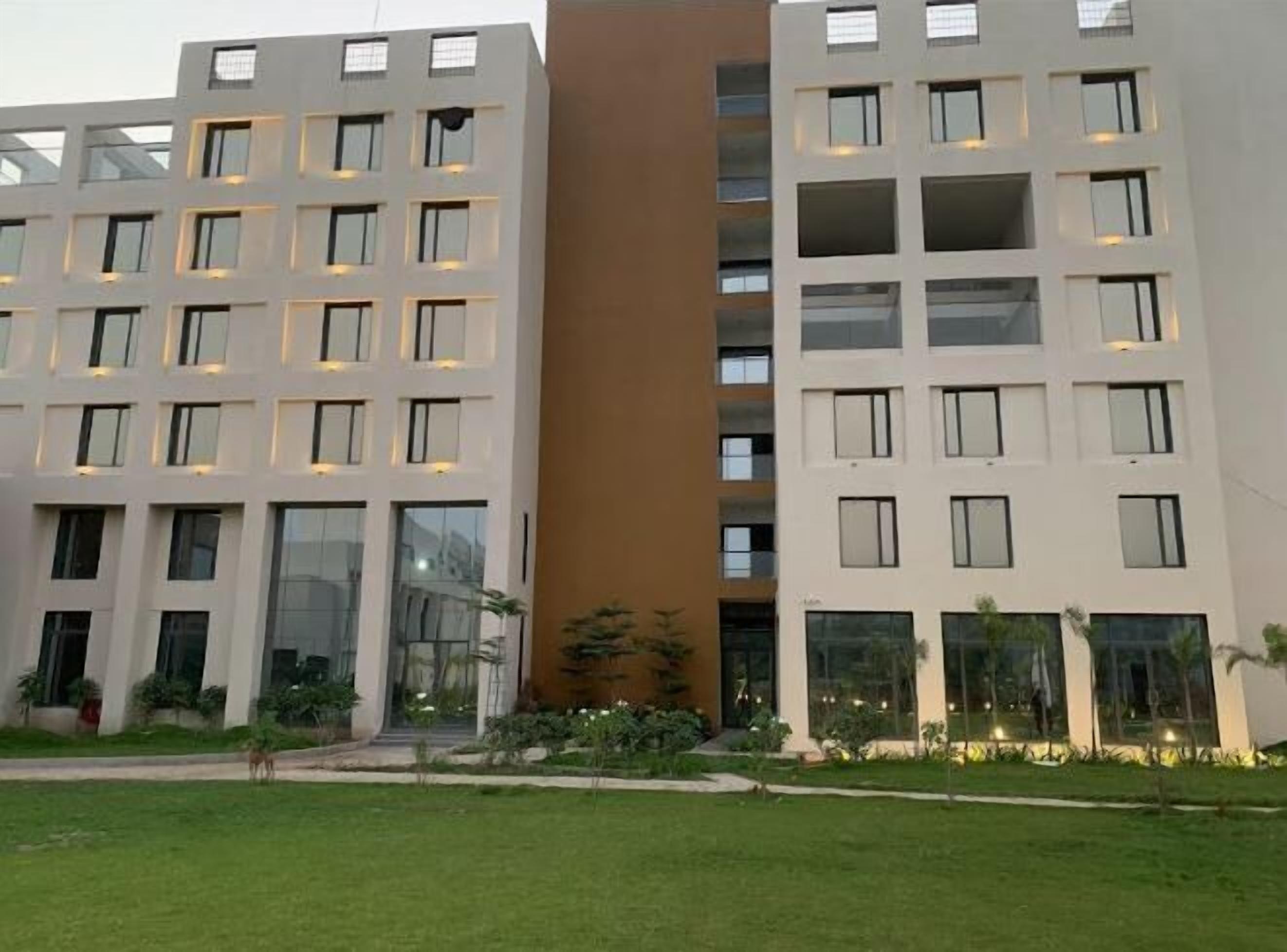 A modern multi-story building with a central brown section, surrounded by white buildings with evenly spaced windows.