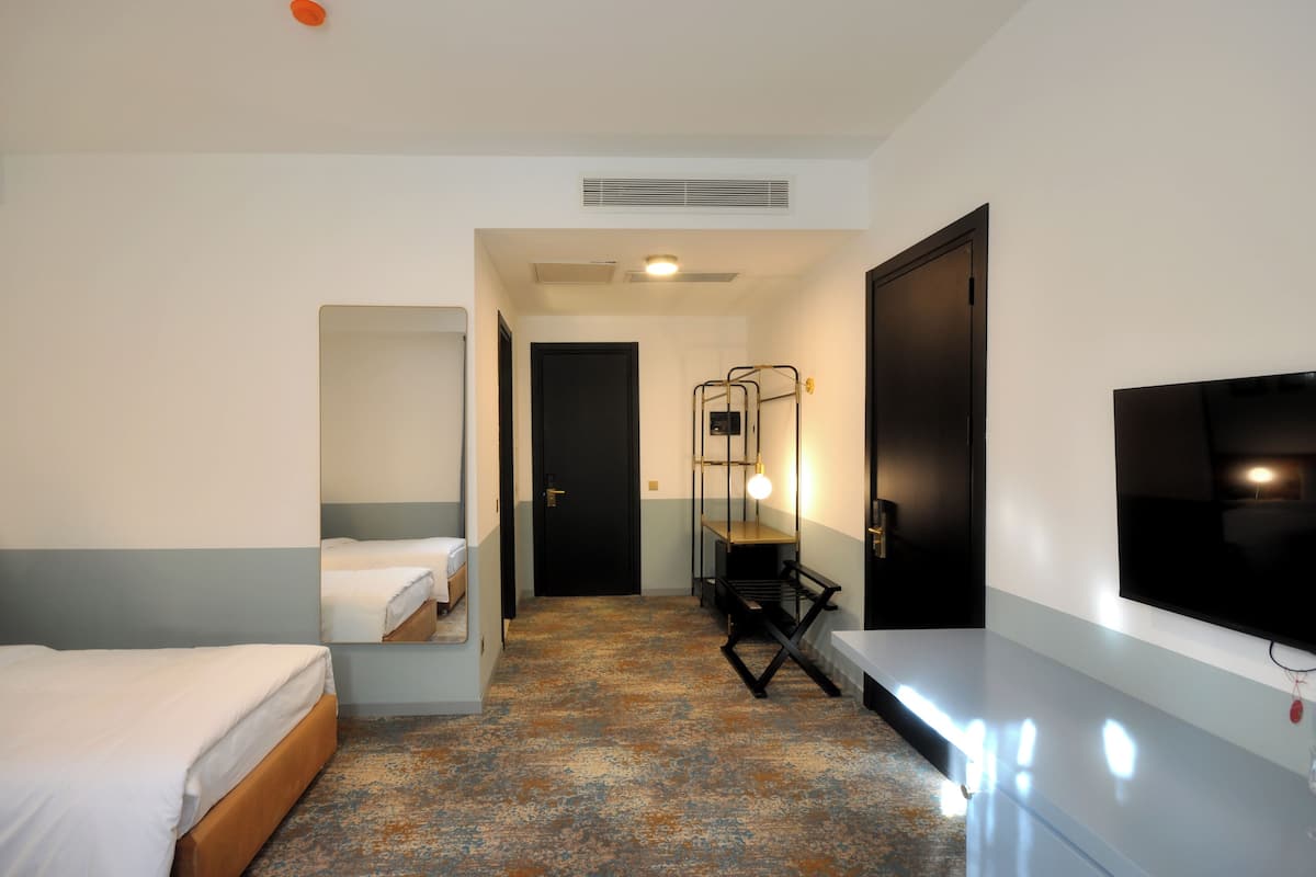 A hotel room with a bed, a bench, a TV, and a door.