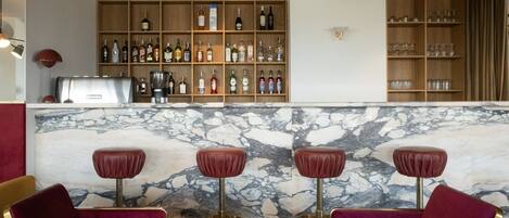 A bar area with marble countertops, red bar stools, and shelves stocked with bottles and glasses.