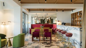 A modern bar area with a marble countertop, red bar stools, and a seating area with green chairs and a table. - Castor & Pollux Hotel (Tbilisi)