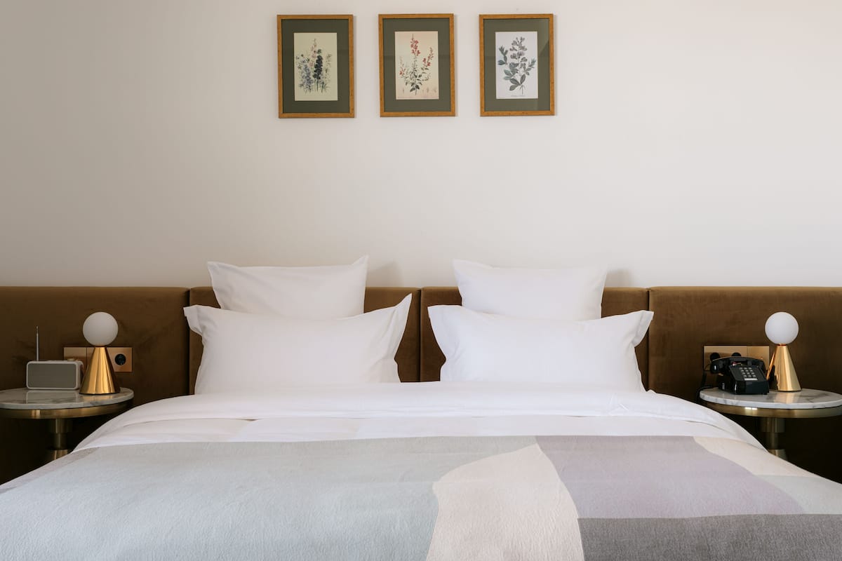 A hotel room with a bed, two bedside tables, a round table, and three framed botanical prints on the wall.