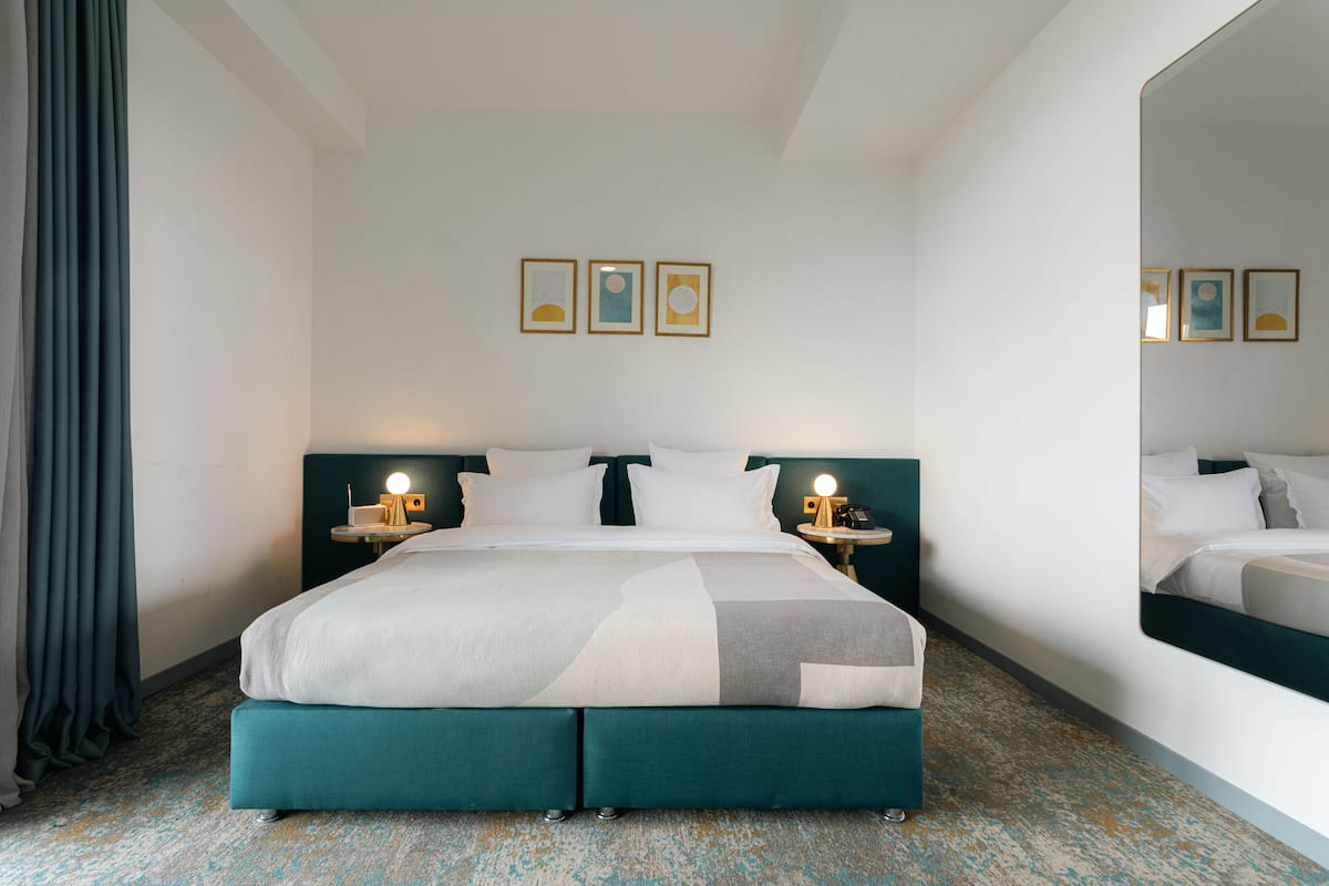 A hotel room with a large bed, two bedside tables with lamps, a mirror, and three framed pictures on the wall.