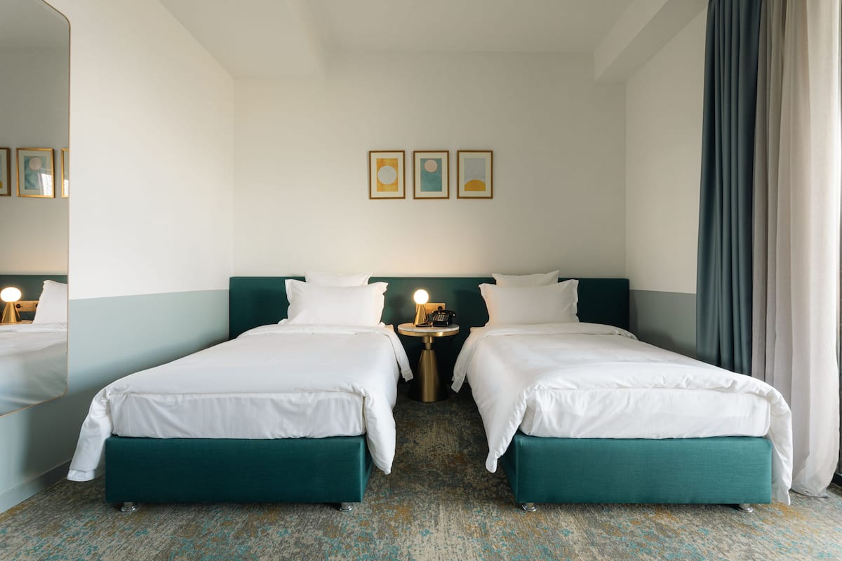 A hotel room with two beds, a nightstand with a lamp, and a wall with three framed pictures.