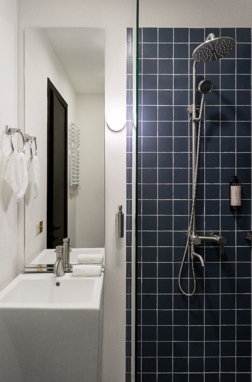 A modern bathroom with a white sink, a mirror, and a shower with a blue tiled wall.