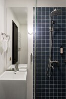 Un baño moderno con lavamanos blanco, espejo y ducha con pared de azulejos azules.