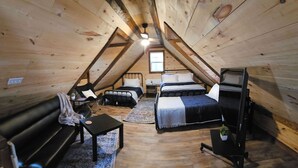 A cozy attic bedroom with a loft bed, a sofa, a desk, and a chair.