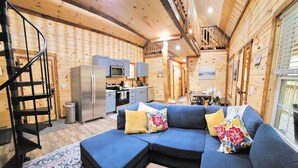 A cozy cabin interior with a living area featuring a sectional sofa, a small table with a remote control, and a patterned rug.
