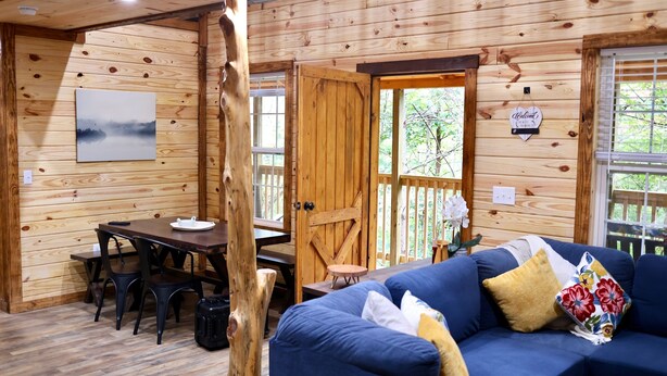 A cozy cabin interior with a dining area, a sofa, and a wooden door leading outside.