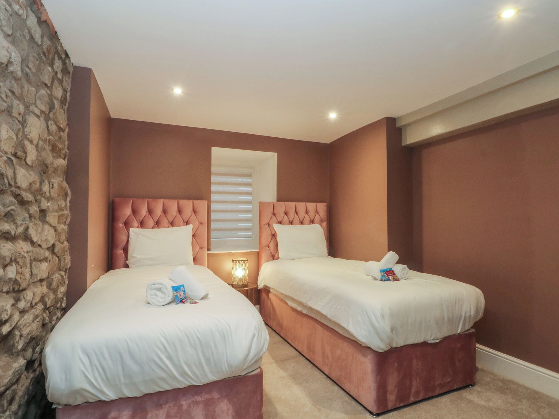 A hotel room with two beds, each with a tufted headboard, white bedding, and a small bedside table with a lamp.