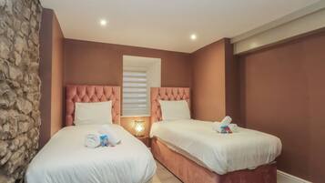 A hotel room with two beds, each with a tufted headboard, white bedding, and a small bedside table with a lamp.