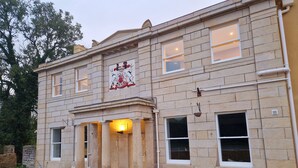 A stone building with a large emblem above the entrance, multiple windows, and a paved walkway.