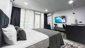 Ein modernes Hotelzimmer mit Bett, Schreibtisch, Sessel und einem Fernseher an der Wand.