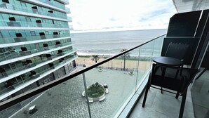 Ein modernes Gebäude mit Glasfassade, das auf einen Strand und einen Hafen mit Booten blickt.