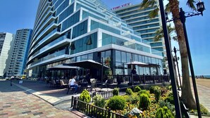 A modern hotel with a glass facade, outdoor seating, and a palm tree.