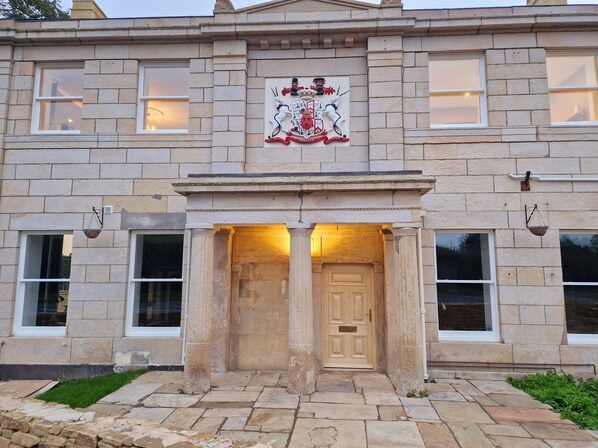 A stone building with a prominent coat of arms above the entrance, featuring a knight and a unicorn.