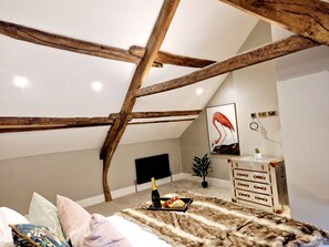 A bedroom with exposed wooden beams, a bed with a fur throw, a bedside table with a plant, and a framed artwork on the wall.