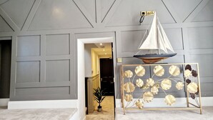 A modern interior with a staircase leading to a dark room, a decorative sailboat, and a gold-framed plant stand. - The Cruck (Preston)