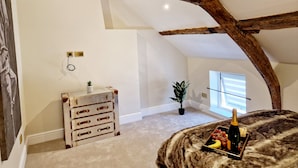 A room with exposed wooden beams, a trunk with drawers, a potted plant, and a table with a bottle and fruit. - The Cruck (Preston)