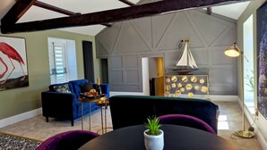 A room with a high ceiling, exposed wooden beams, a blue sofa, a small round table with a plant, and a decorative sailboat. - The Cruck (Preston)