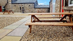 An outdoor patio area with stone walls, a wooden picnic table, and a stone fountain. - The Cruck (Preston)