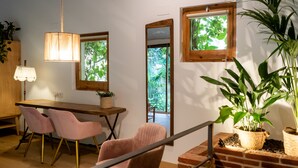 A modern interior with a wooden dining table, pink chairs, a hanging light fixture, and a brick accent wall.