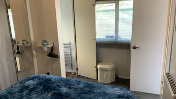 A bedroom with a large bed, a small bathroom, and a window with blinds.