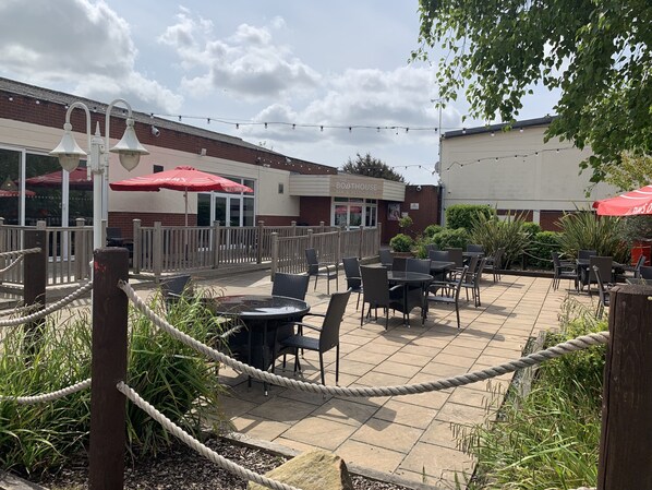 An outdoor patio area with tables and chairs, surrounded by a rope barrier, and a building with a sign reading "The Boathouse Bar & Restaurant" in the background. - Immaculate 2-bed Caravan in Clacton-on-sea (Clacton-on-Sea)
