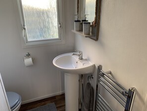 A bathroom with a white sink, a toilet, a window, and a towel rack. - Immaculate 2-bed Caravan in Clacton-on-sea (Clacton-on-Sea)