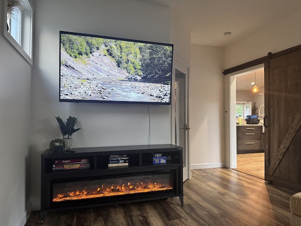 A living room with a flat-screen TV mounted on the wall, a fireplace below it, and a wooden floor. - Central location | Hot Tub | Heated Pool | Digital Game Table (Normal)