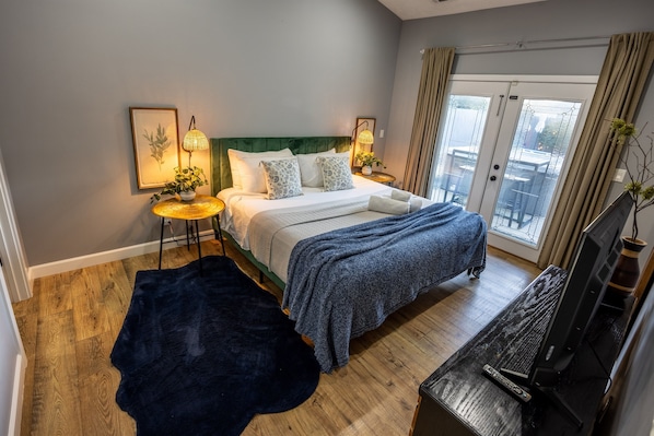 A bedroom with a bed, bedside tables, a TV, and a view of the outdoors.