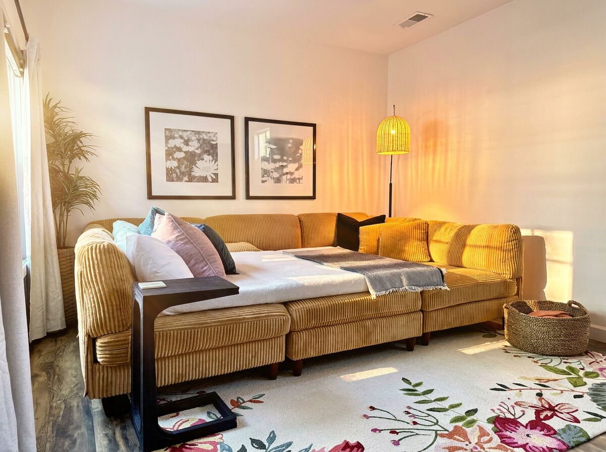 A living room with a sofa, a floor lamp, framed pictures on the wall, and a floral rug.