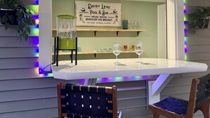 A dining area with a table, chairs, a sign reading "Daisy Lane Pool & Bar", and a water feature. - Central location | Hot Tub | Heated Pool | Digital Game Table (Normal)