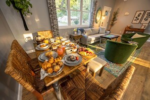A dining area with a wooden table set for breakfast, surrounded by wicker chairs and a green armchair. - Central location | Hot Tub | Heated Pool | Digital Game Table (Normal)