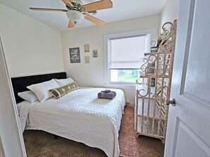 Ein Schlafzimmer mit Bett, Deckenventilator, Fenster mit Jalousien und einem dekorativen Gitter.