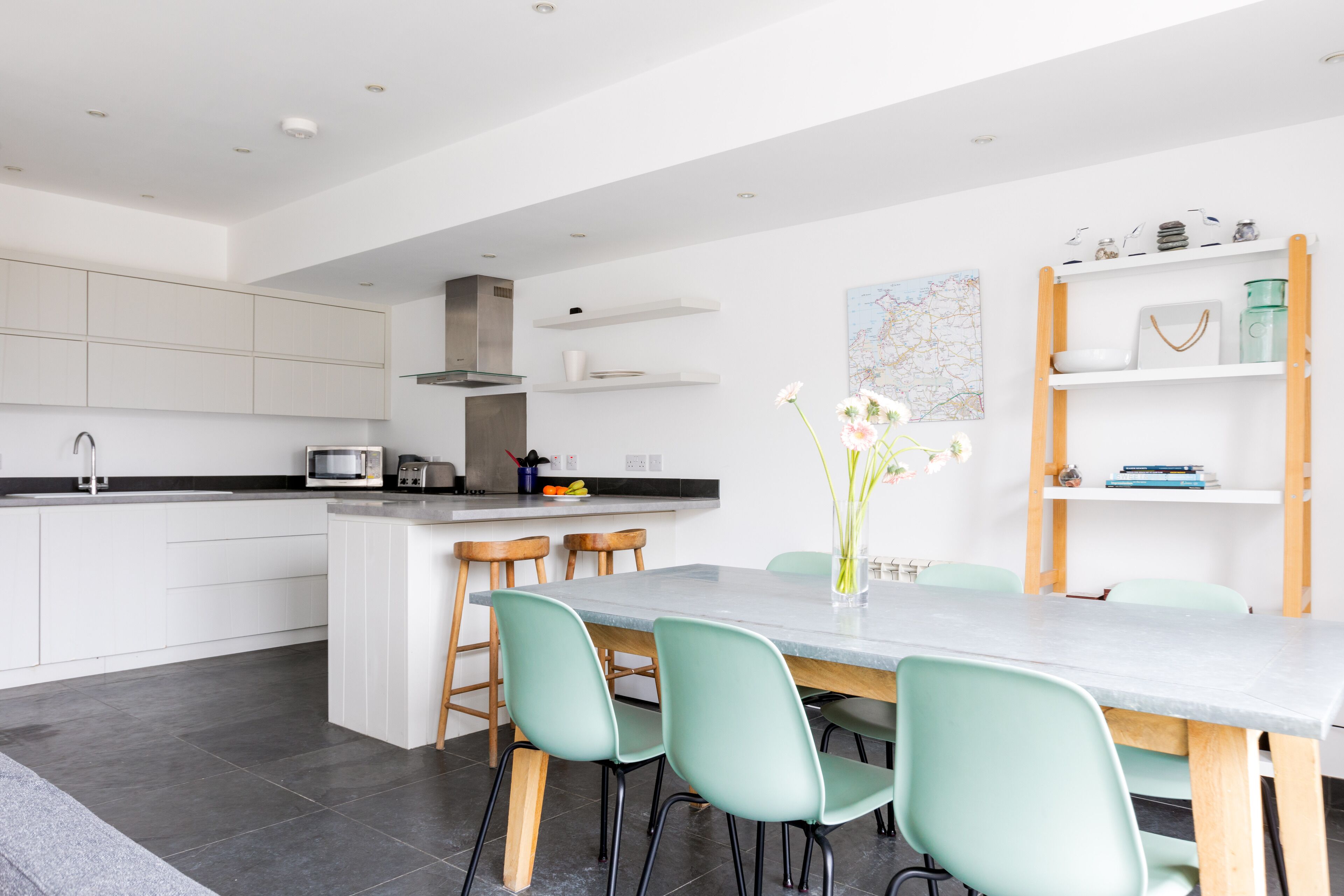 A modern kitchen with white cabinets, a central island with stools, and a dining area with a marble table and green chairs.