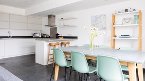 Une cuisine moderne avec des meubles blancs, un îlot central doté de tabourets et un coin repas avec une table en marbre et des chaises vertes.