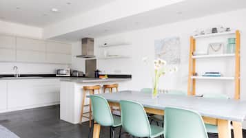 A modern kitchen with white cabinets, a central island with stools, and a dining area with a marble table and green chairs.